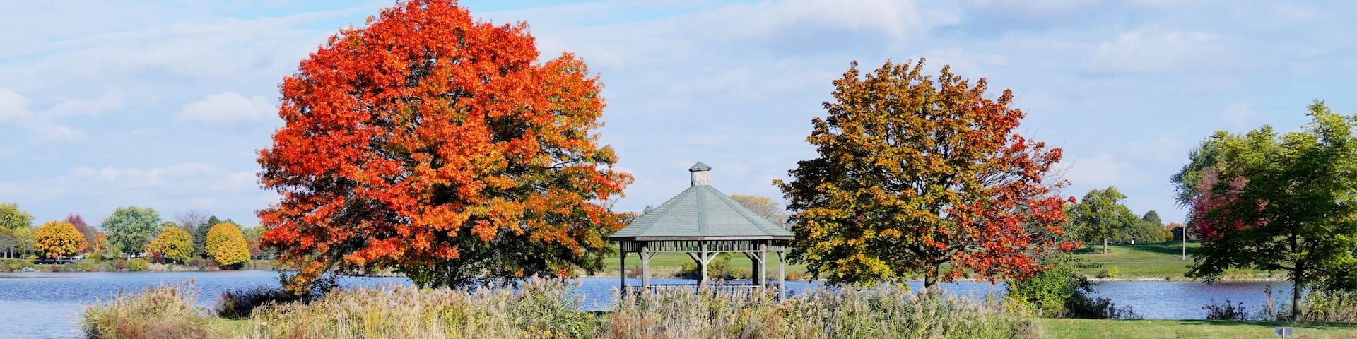 A serene lake with autumn foliage, a gazebo, and a clear reflection.