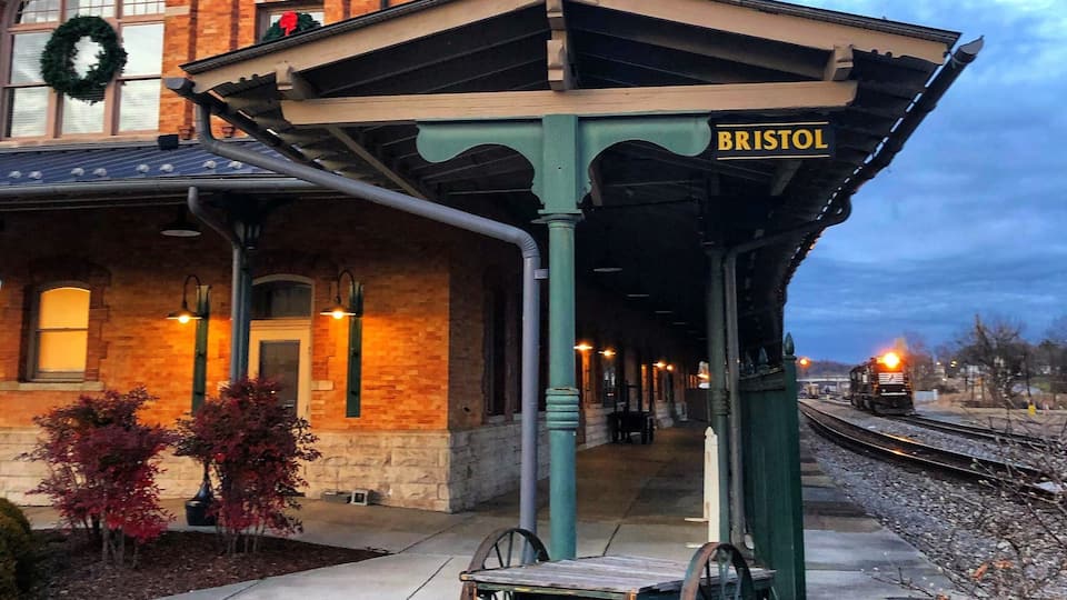 A train station named Bristol with a brick building, a covered waiting area, and a train on the tracks.