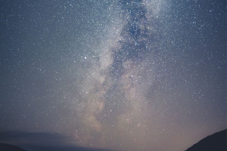 A starry night sky over a mountainous landscape with a lake.