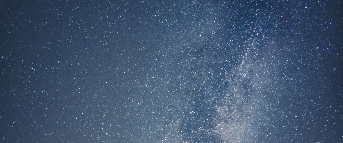 A starry night sky over a mountainous landscape with a lake.