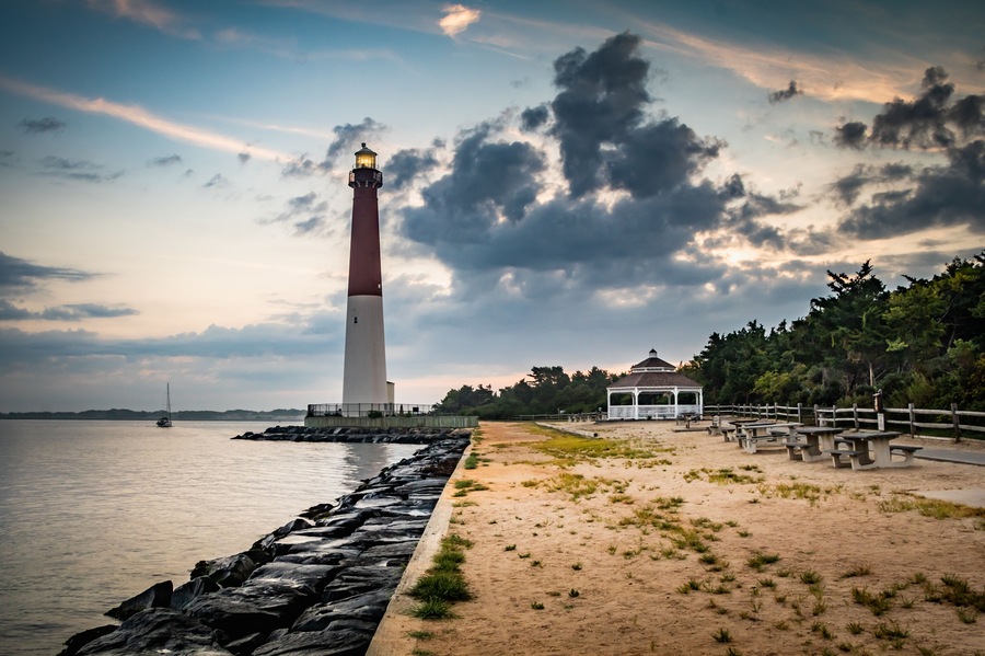 Ein Leuchtturm, ein Sandstrand, eine Holzzahlung und ein Pavillon am Wasser.