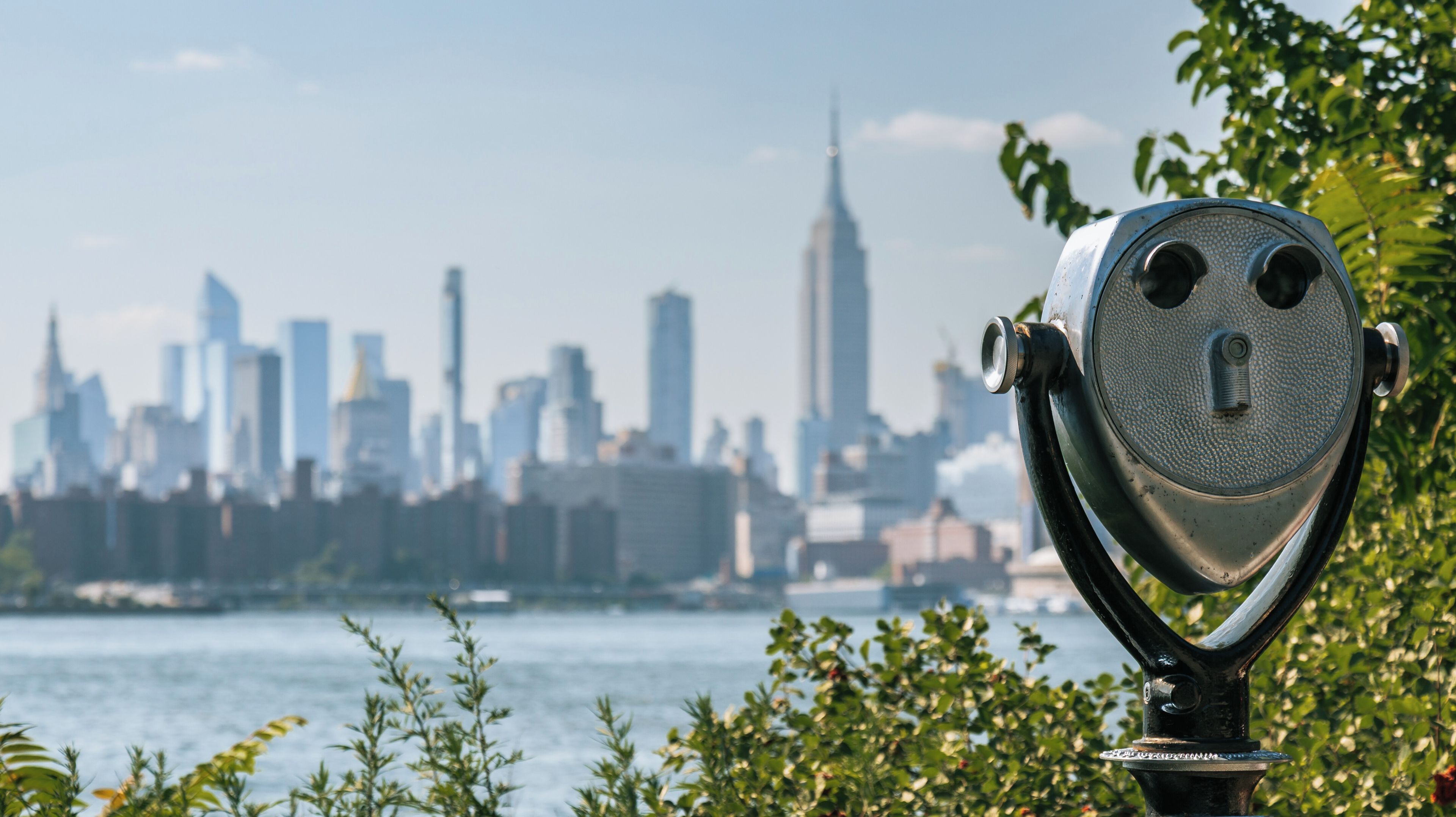 A telescope overlooking a city skyline with prominent skyscrapers, including a tall, pointed building.