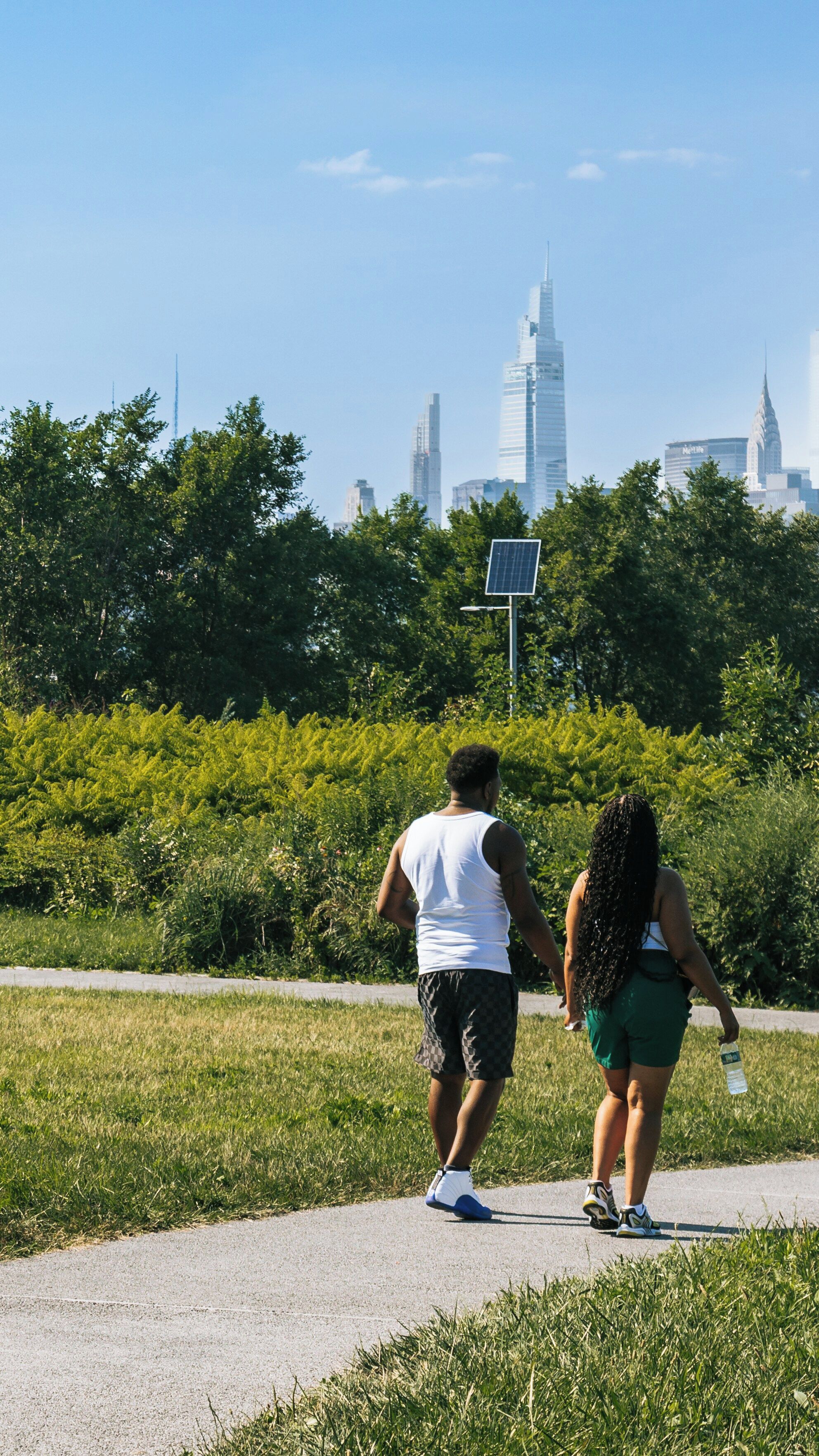 Two people walking on a path with a city skyline in the background.