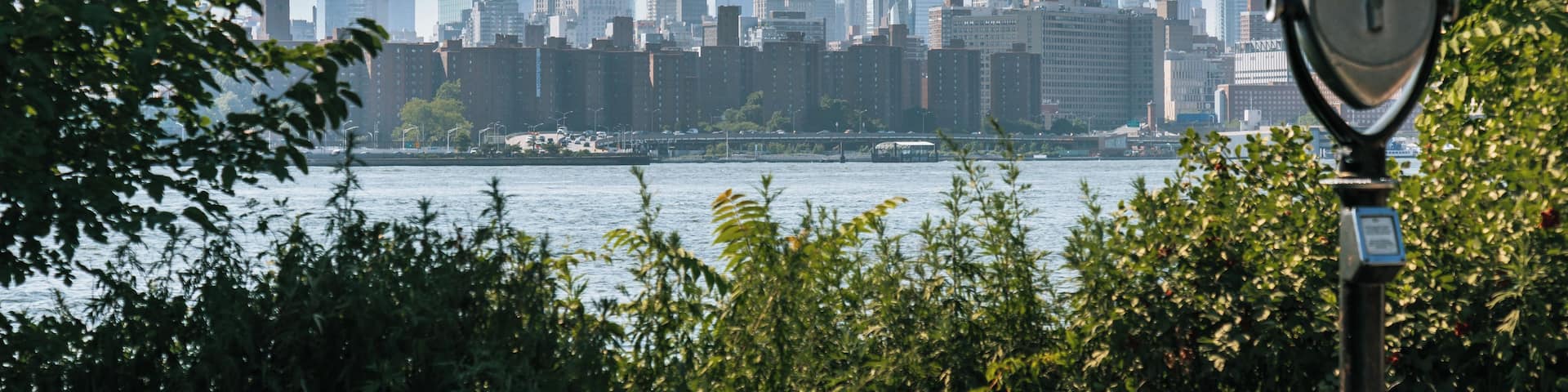 A city skyline with modern skyscrapers, a river, and a park with a telescope.