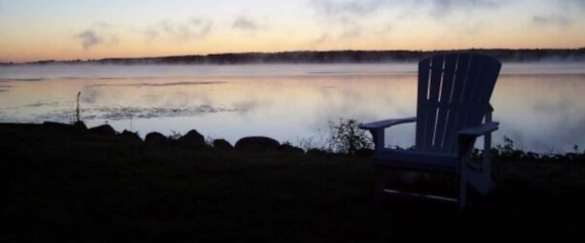 A chair by a calm lake at dusk.