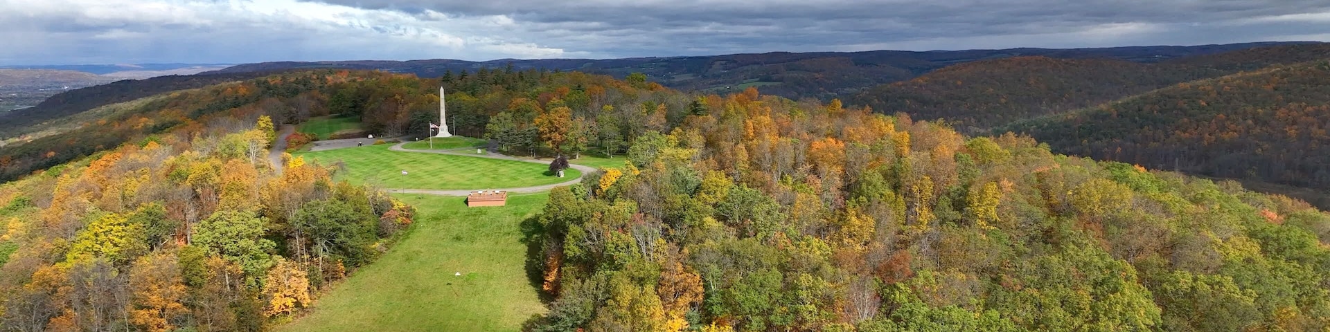 Historic Revolutionary War monument at Newtown Battlefield State Park with American flag blowing in the wind on hillside in New York State during Autumn Fall season color