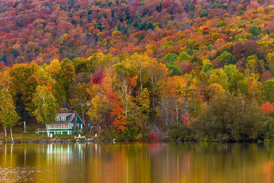 A house by a lake surrounded by autumn-colored trees.