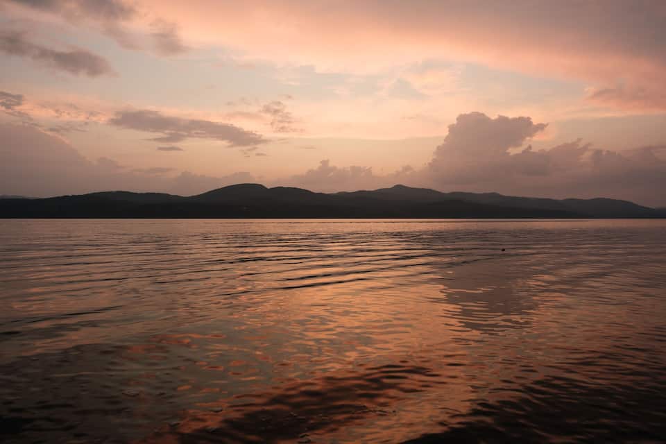 A sunset over a calm lake with mountains in the background.