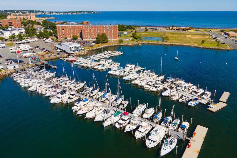 A marina with numerous boats docked, a large building, and a view of the ocean.