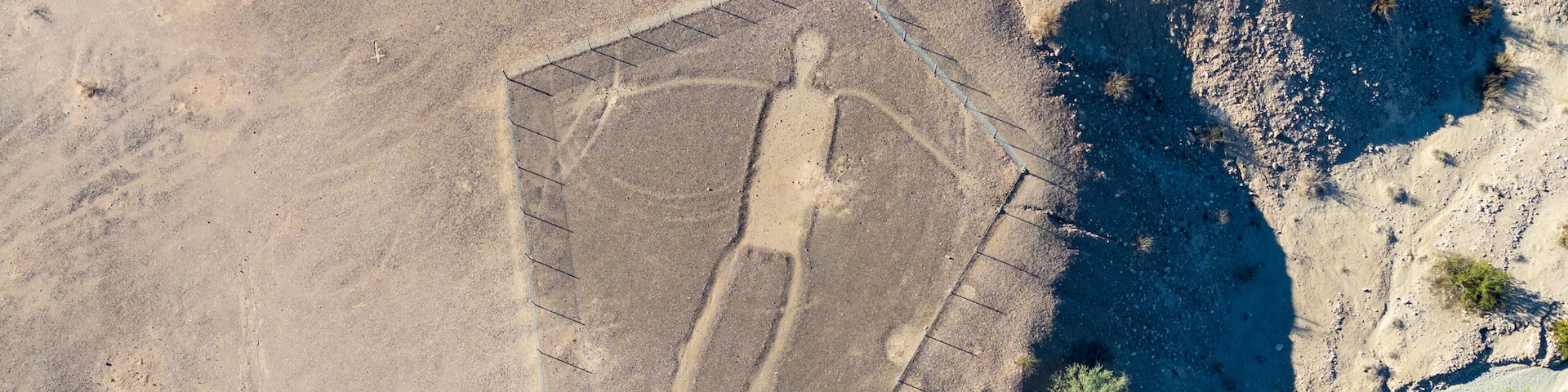 Blythe Intaglios Aerial View – Main Human Geoglyph, California Desert. Ancient desert figure near Blythe with visible erosion channel approaching fence, showing natural wear over time.