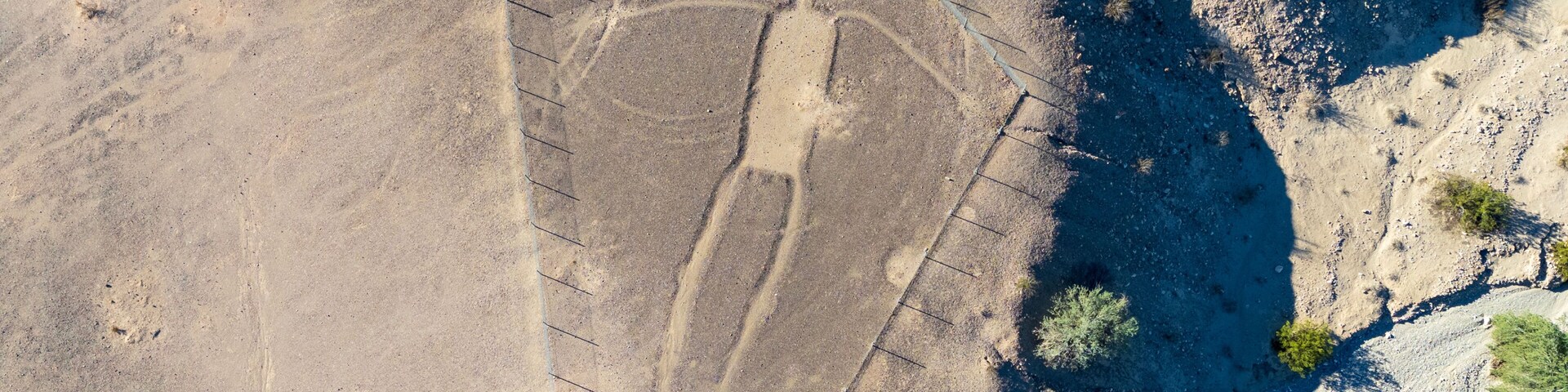 Blythe Intaglios Aerial View – Main Human Geoglyph, California Desert. Ancient desert figure near Blythe with visible erosion channel approaching fence, showing natural wear over time.