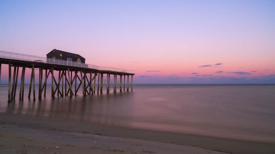 A pier extending into calm waters at dusk with a small building at the end.
