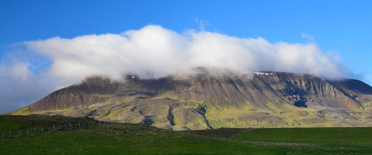 A mountain with a grassy foreground and a partly cloudy sky.