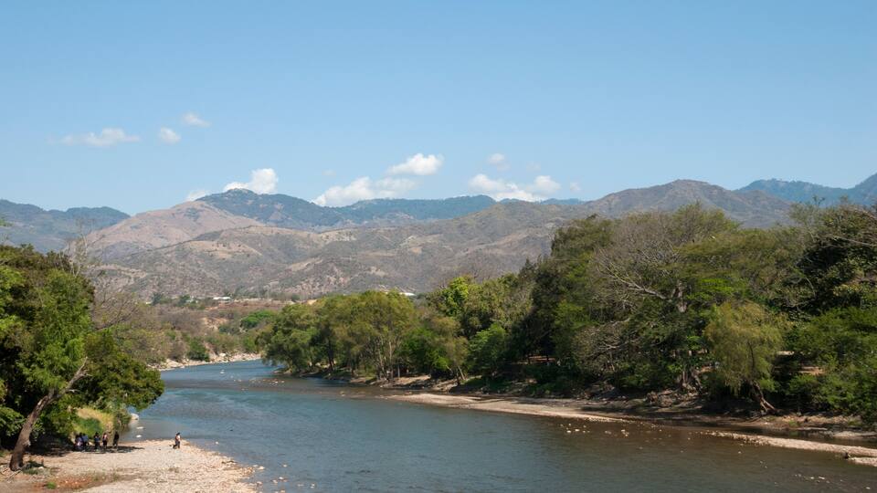 A river flowing through a mountainous landscape with trees and a clear sky.