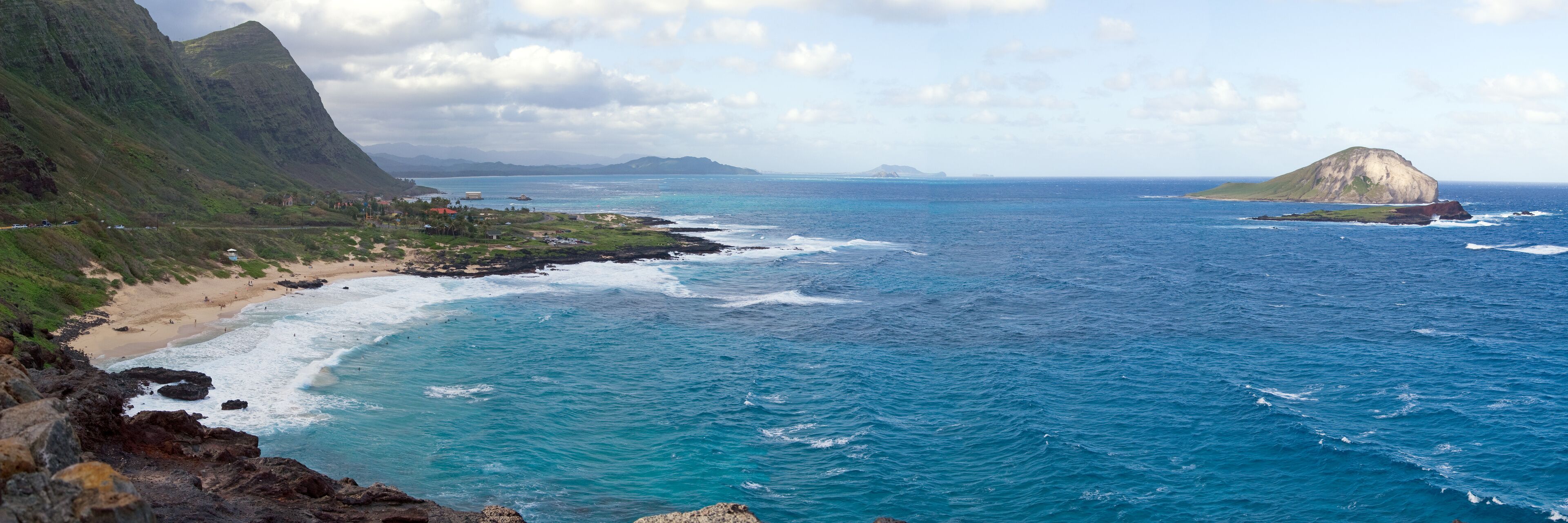 A coastal landscape with a beach, rocky coastline, and a prominent hill.
