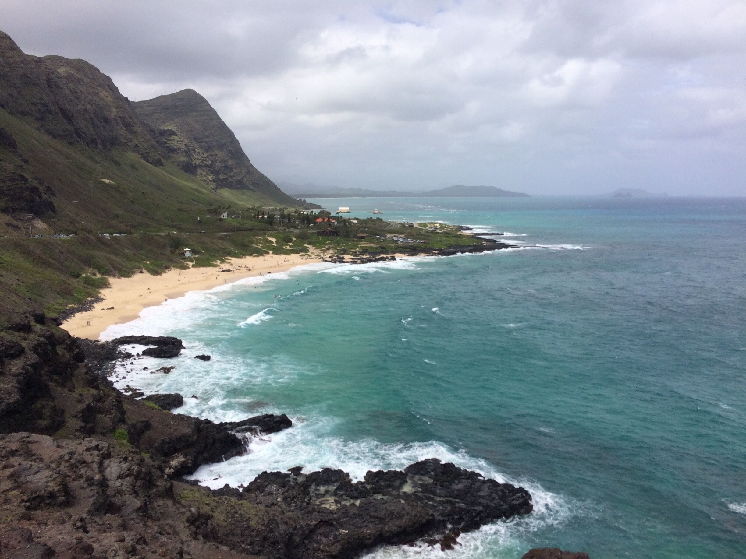 A coastal landscape with a sandy beach, rocky shoreline, and a mountainous backdrop.