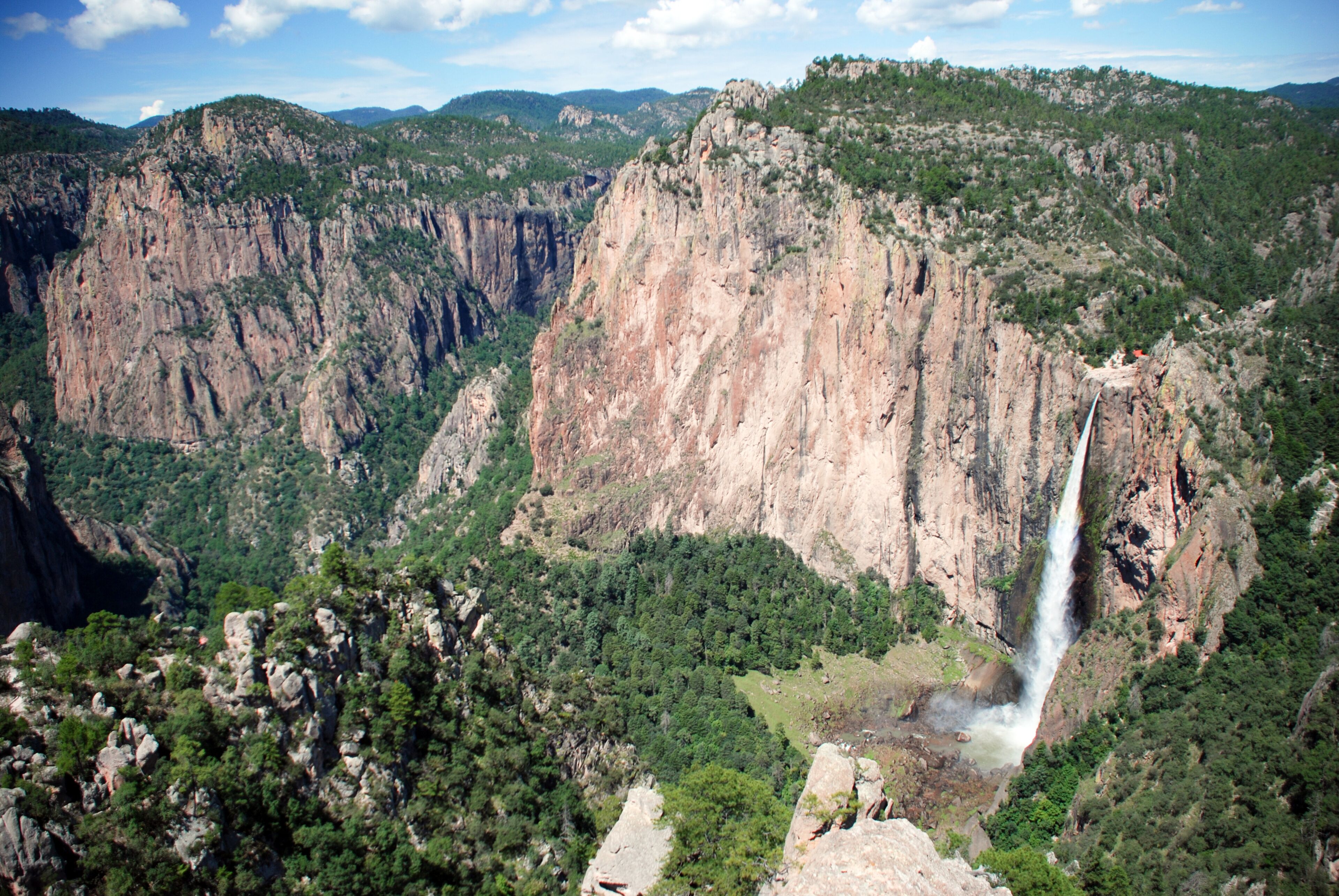 A canyon with a waterfall, steep cliffs, and dense greenery.