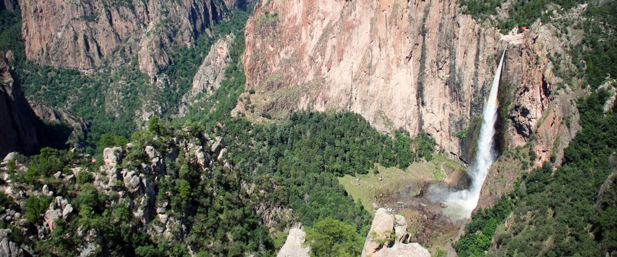 A canyon with a waterfall, steep cliffs, and dense greenery.