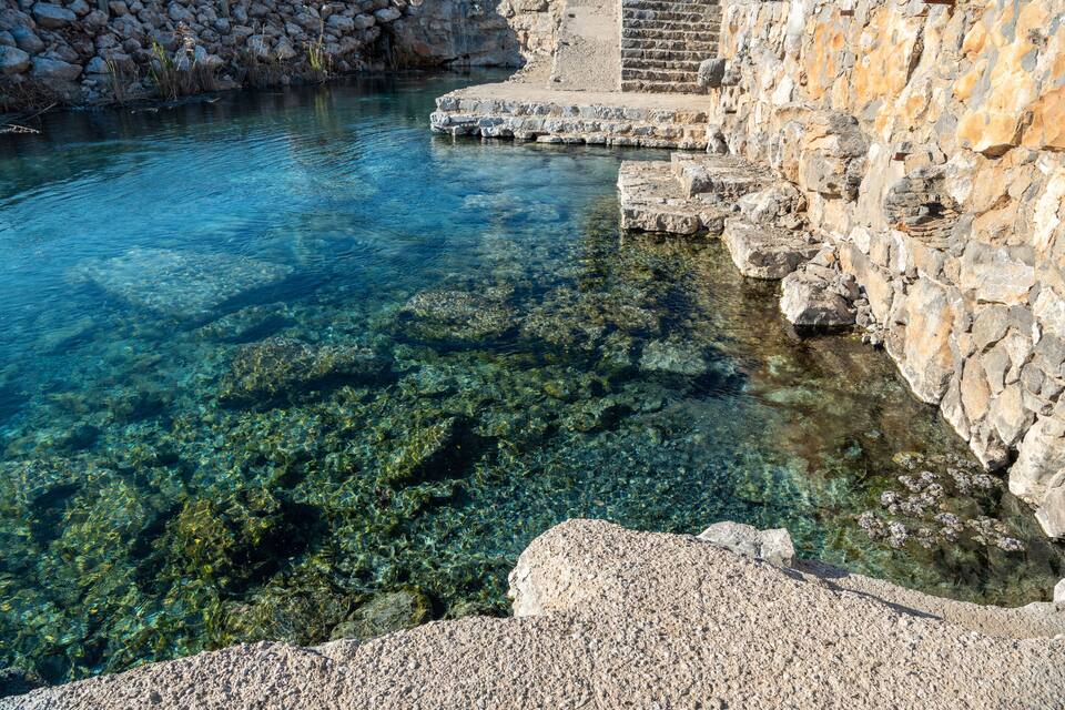 A clear pool with visible underwater rocks and a stone wall.