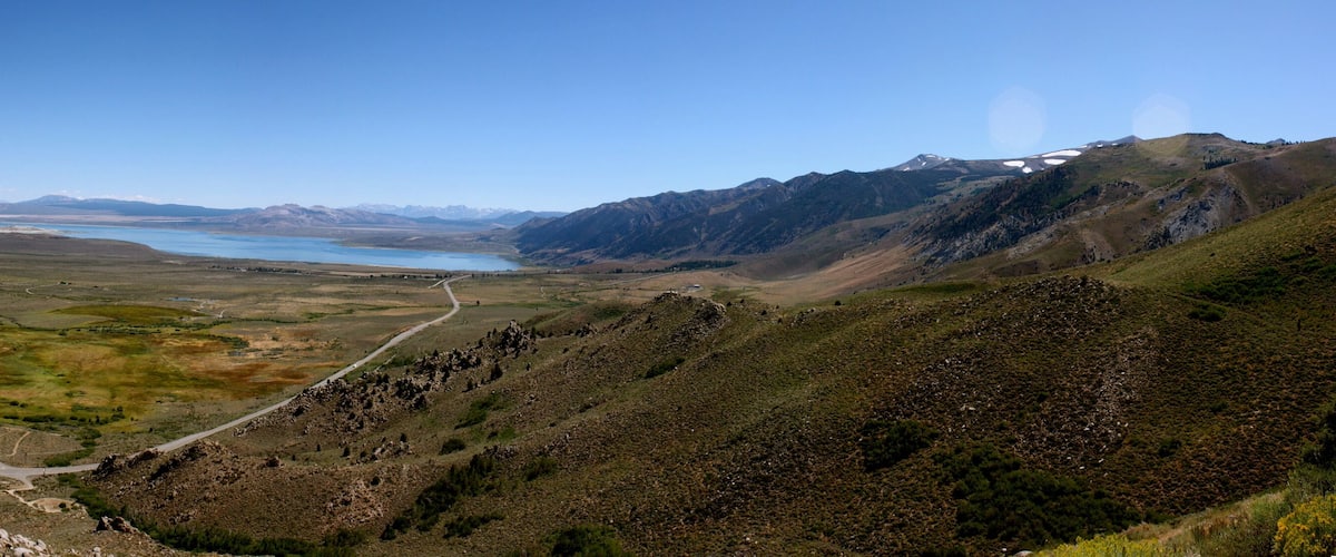 A mountainous landscape with a winding road, a large lake, and distant snow-capped peaks.