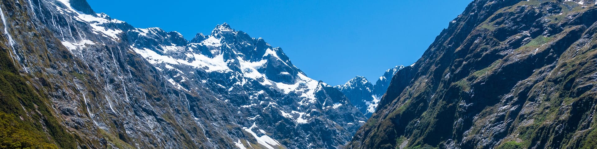 A mountainous landscape with a clear blue lake surrounded by rocky terrain and snow-capped peaks.