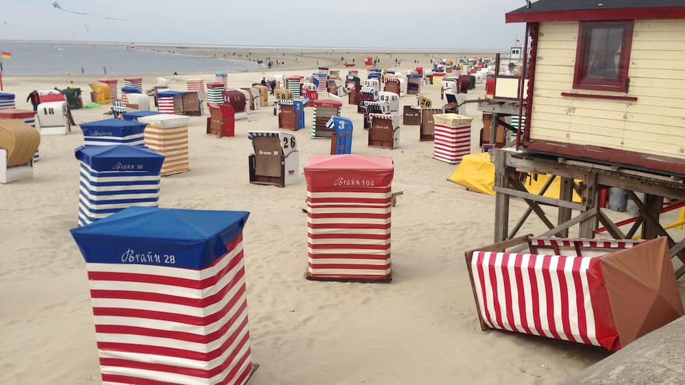 Ein Strand mit zahlreichen gestreiften Liegestühlen und einem Rettungsturm mit der Aufschrift 'Strandkorb'.
