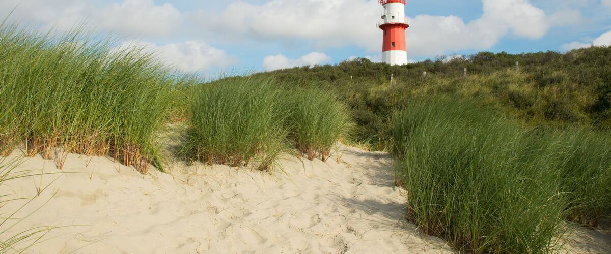 A red and white lighthouse on a sandy dune with green grass.