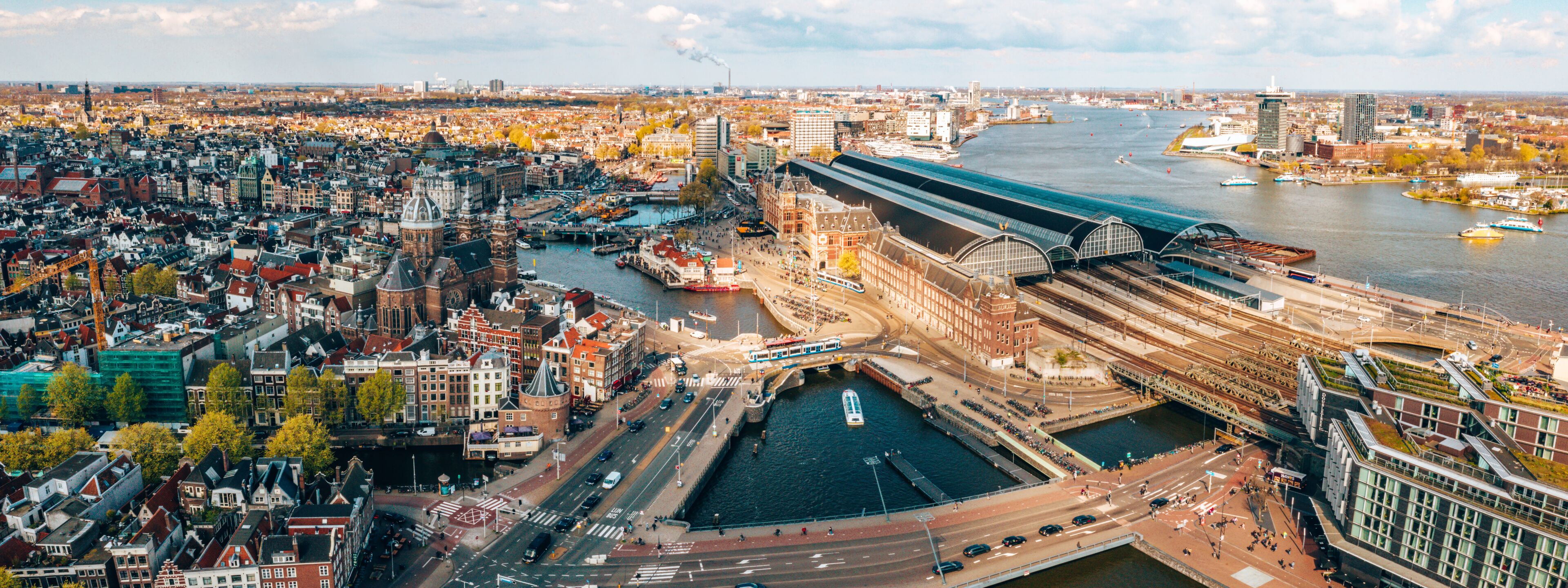 A panoramic view of a historic city with a prominent train station, a river, and dense urban architecture.