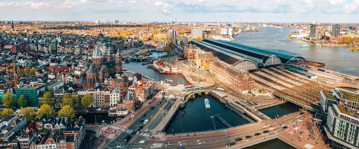 A panoramic view of a historic city with a prominent train station, a river, and dense urban architecture.
