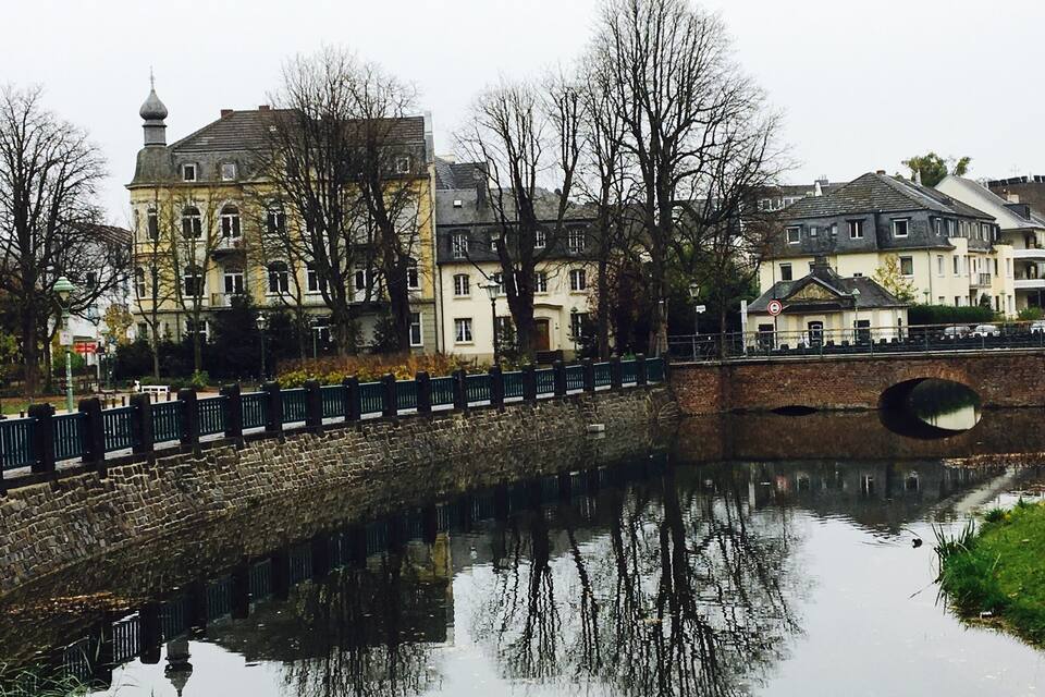 A stone bridge over a calm river, reflecting surrounding buildings and trees.