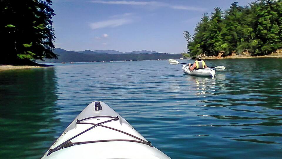 A kayak on calm water with a forested shoreline and distant mountains.