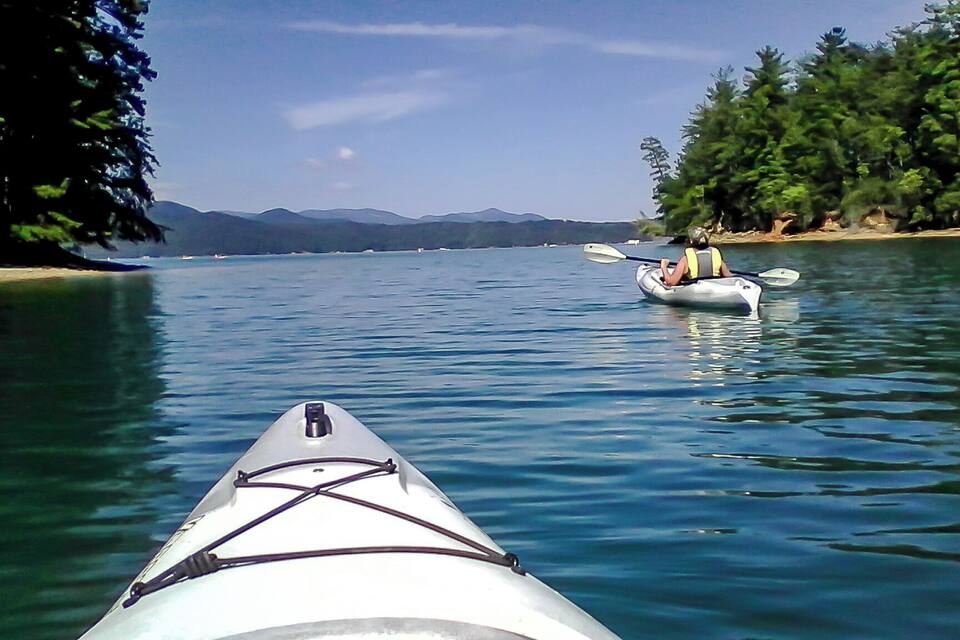 Un kayak sur une étendue d’eau calme, avec une rive bordée d’arbres et des montagnes qui se dessinent à l’horizon.