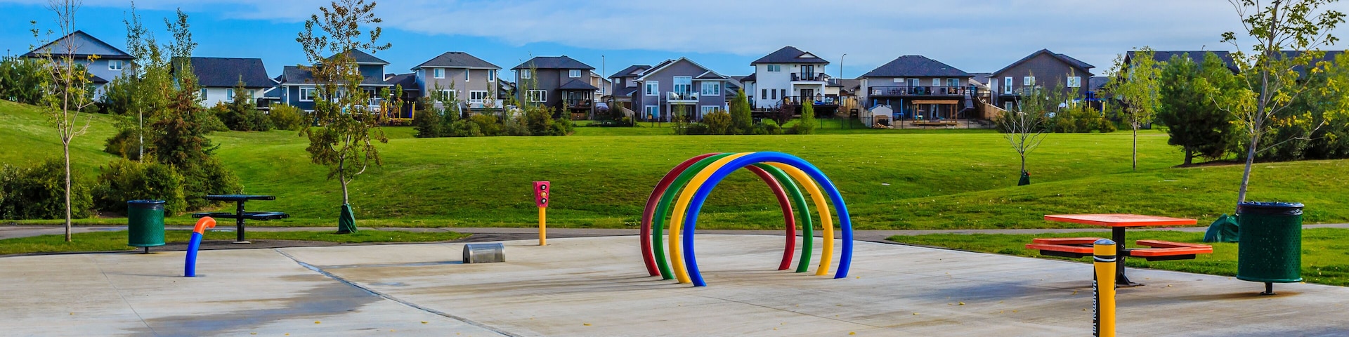 Un parque infantil con anillos de colores, una mesa de picnic y casas al fondo.