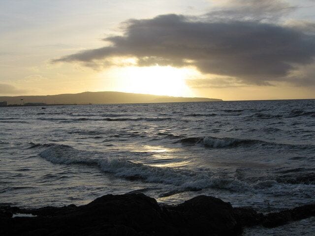 A sunset over the ocean with waves crashing onto rocks.
