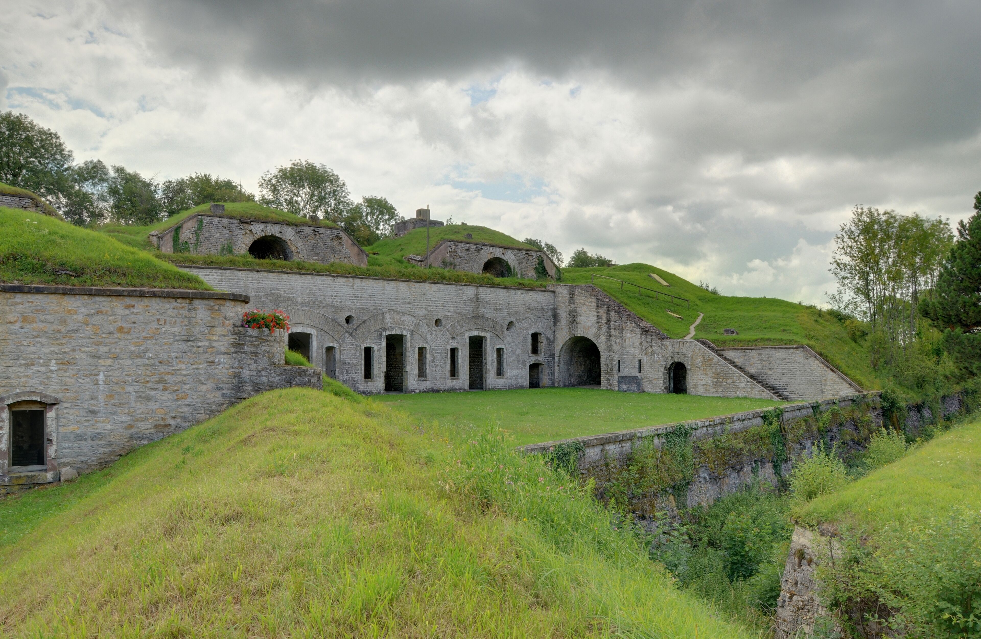 A historic stone building with arched windows and a grassy hill.