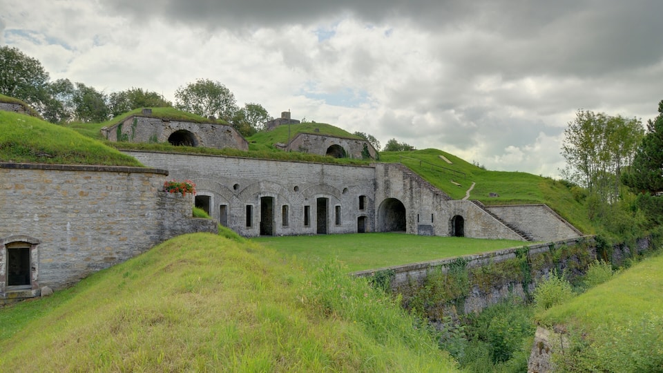 A historic stone building with arched windows and a grassy hill.