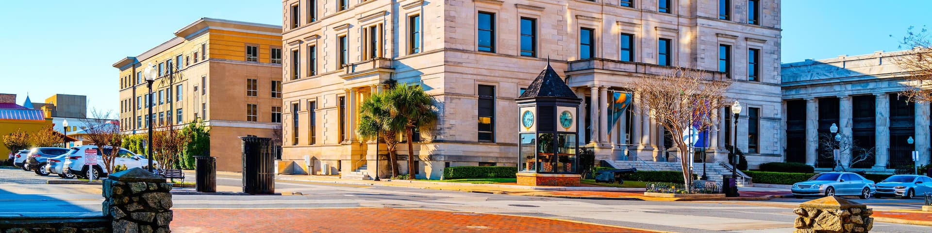A historic building with classical architecture, a street with cars, and a clear blue sky.