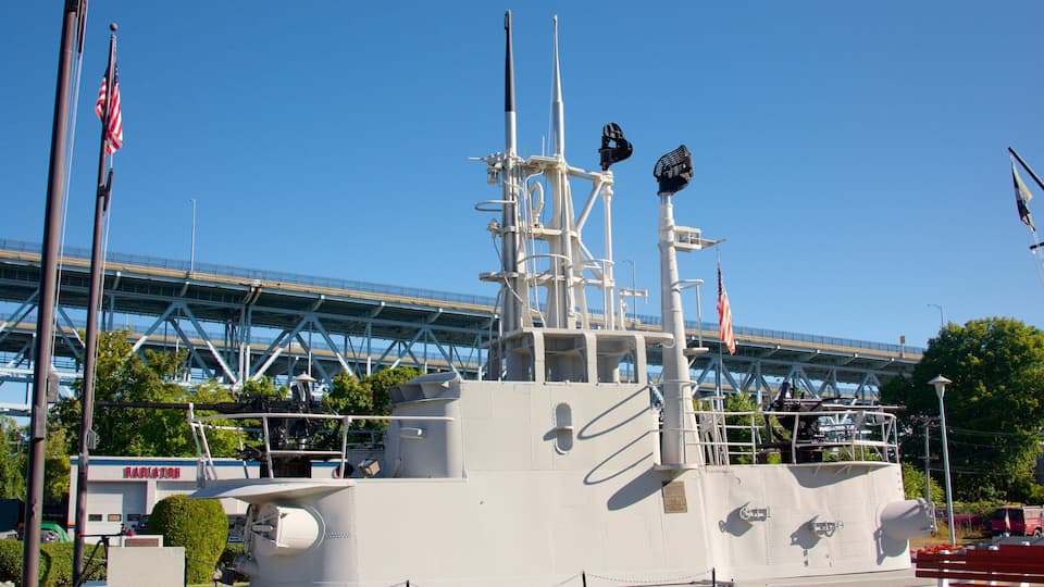 A naval ship docked in a harbor with a bridge in the background.