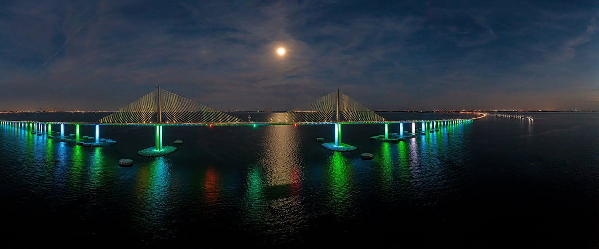 A bridge with illuminated green lights at night, reflecting on the water.