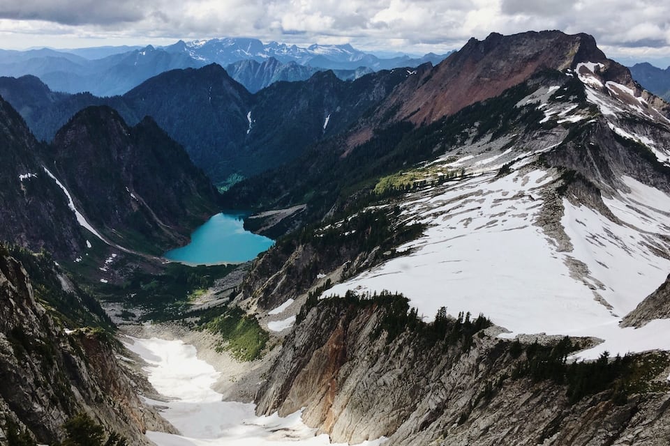 A mountain landscape with a lake, snow-covered peaks, and a valley.