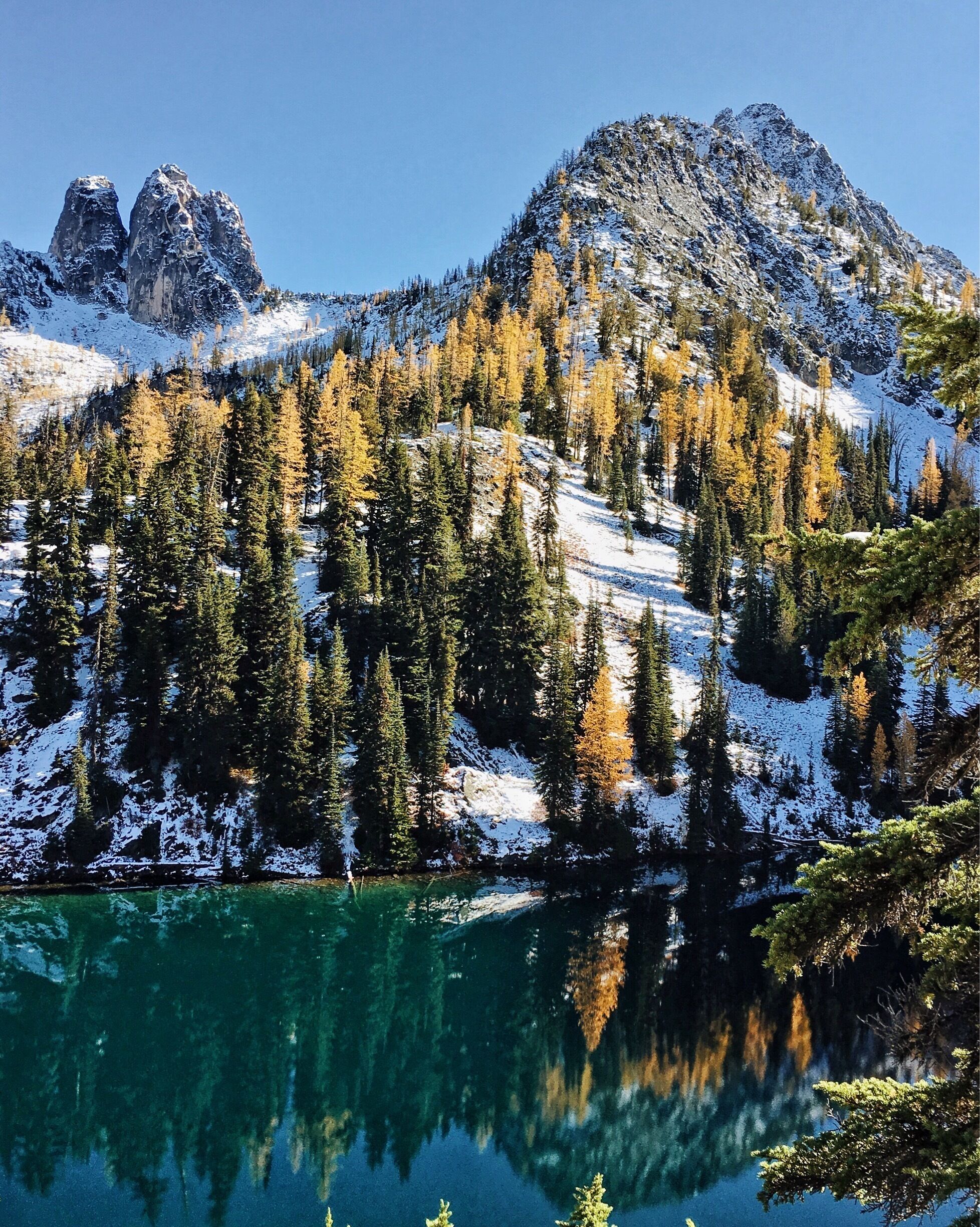 Un paysage de montagne avec des sommets enneigés, un lac d’un bleu limpide et une forêt de conifères dense.