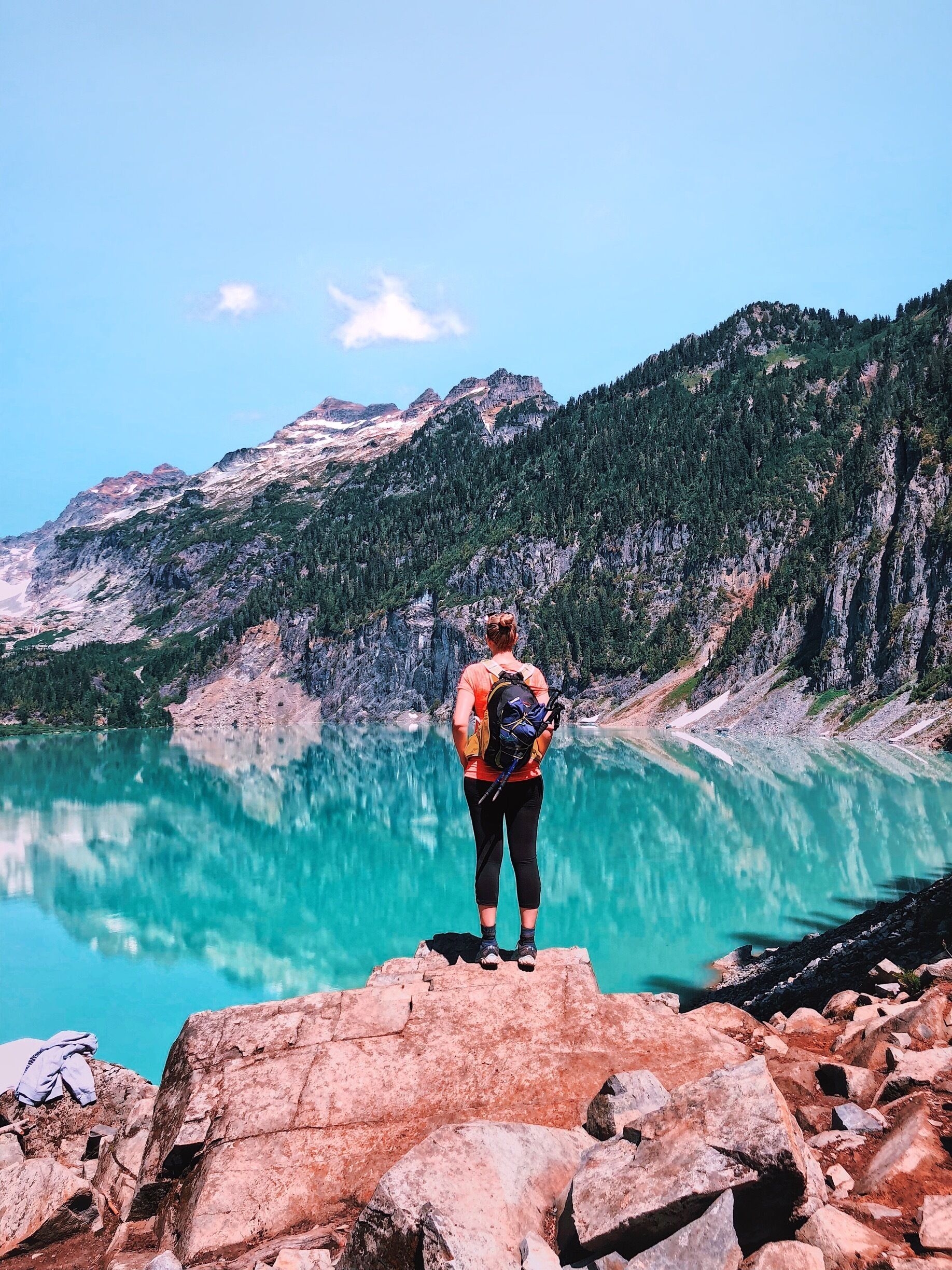 Una persona de pie sobre un promontorio rocoso con vistas a un lago turquesa y montañas al fondo.