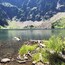 Un lago tranquilo rodeado de montañas, con aguas cristalinas y algo de madera a la orilla.