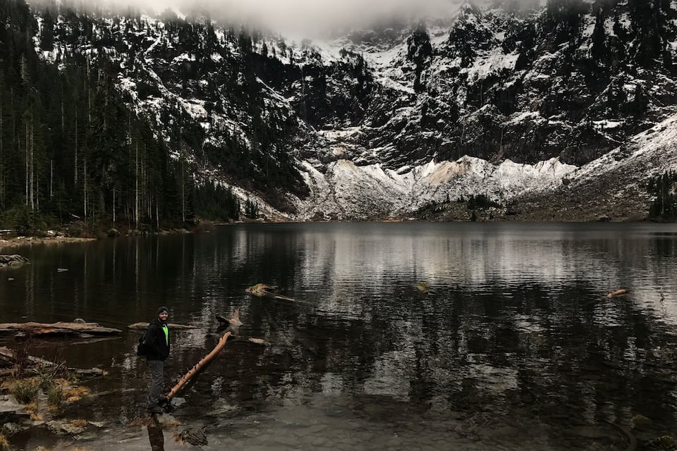 Um lago tranquilo rodeado por montanhas cobertas de neve e uma floresta densa.