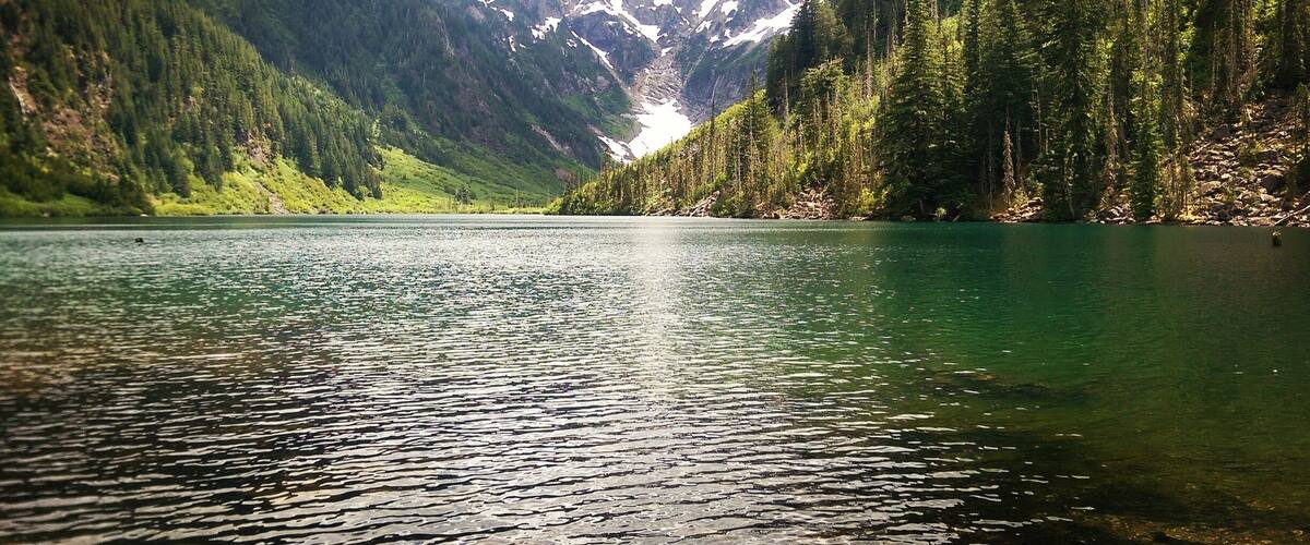 Un lago tranquilo rodeado de densos bosques y montañas nevadas.