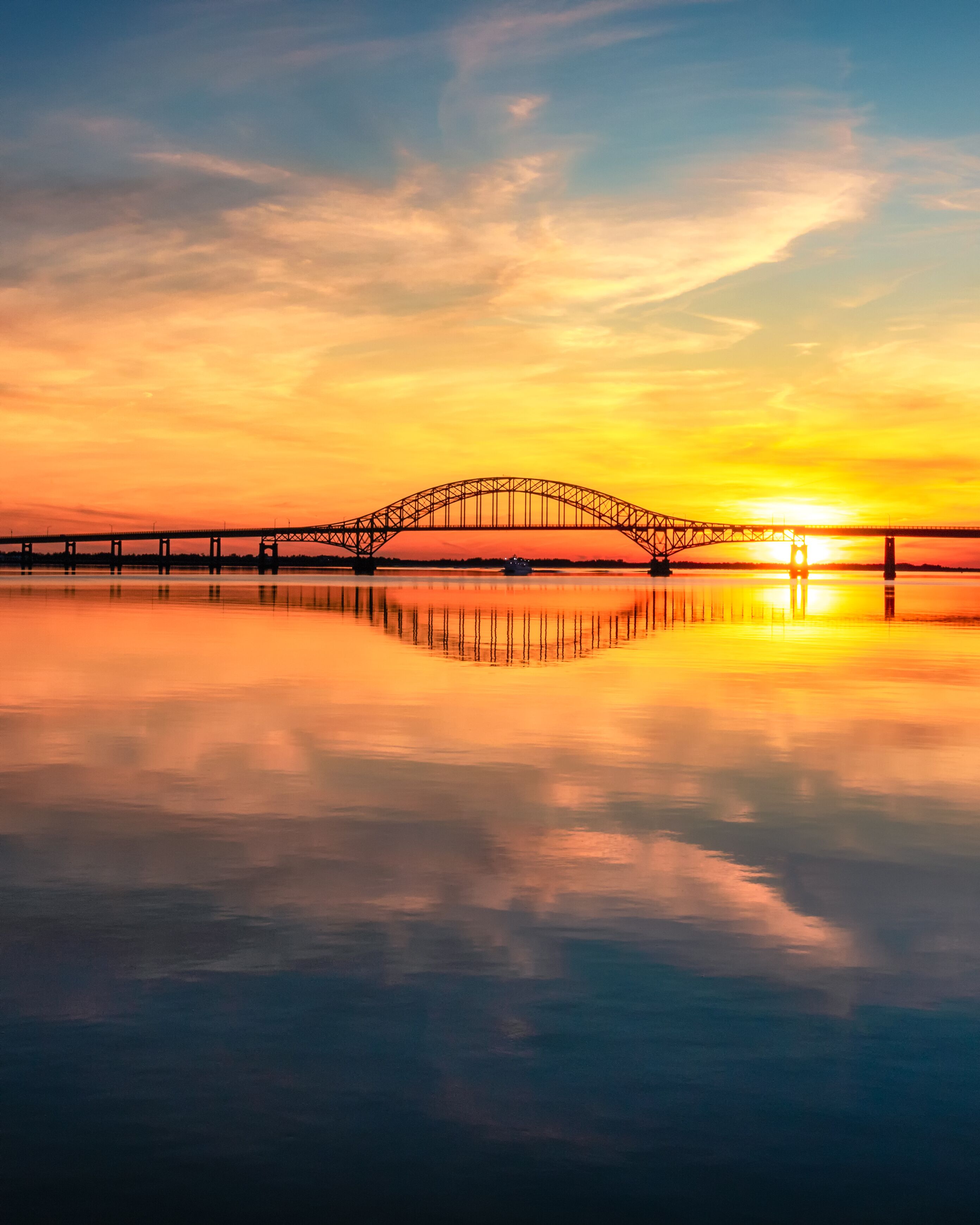 Un puente colgante al atardecer, con un río tranquilo que refleja el cielo.