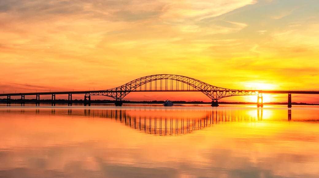 A suspension bridge at sunset with a calm river reflecting the sky.