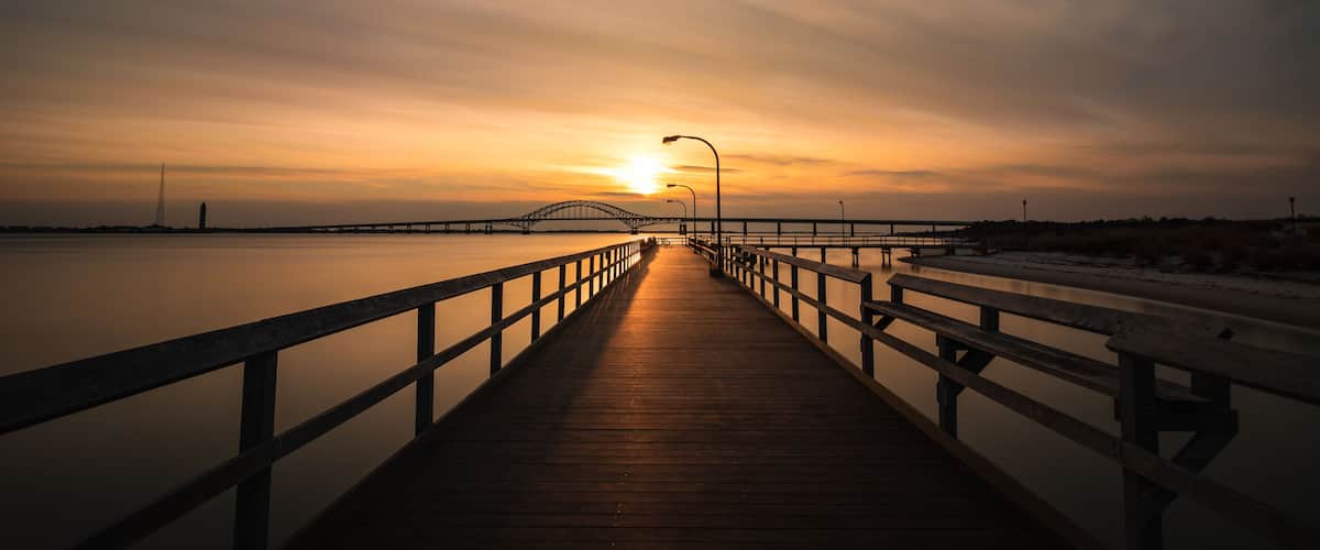 Boardwalk pathway bathed in golden light as the sun sets on the horizon. Fishing pier at Captree State Park, Long Island New York
