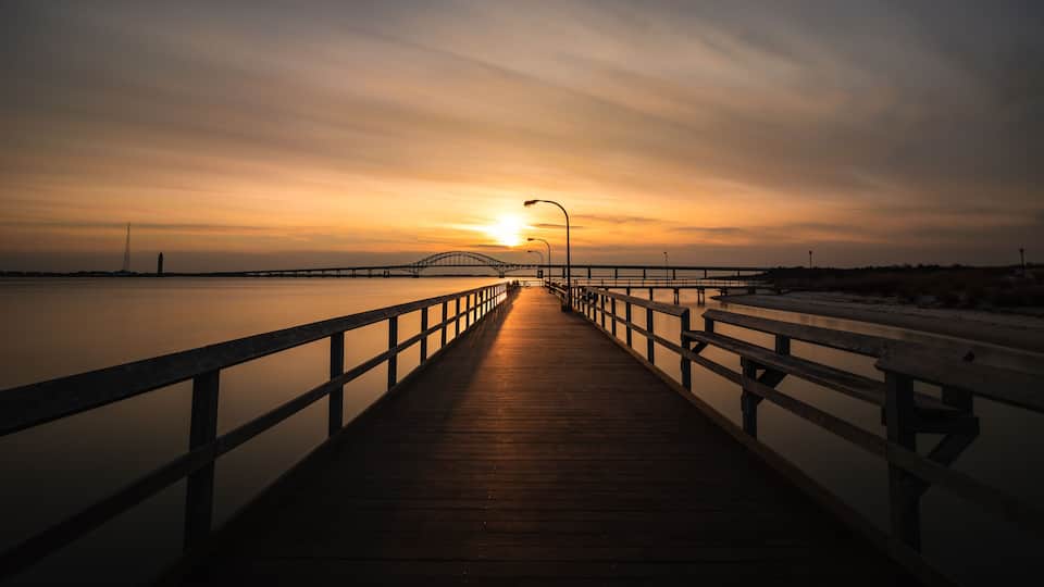 Boardwalk pathway bathed in golden light as the sun sets on the horizon. Fishing pier at Captree State Park, Long Island New York