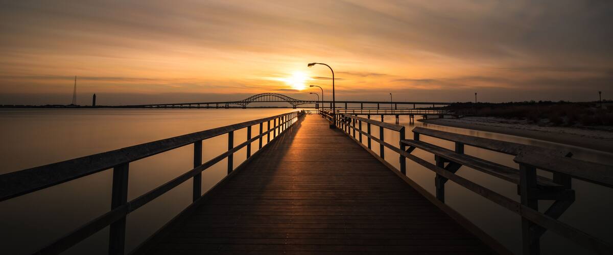 Boardwalk pathway bathed in golden light as the sun sets on the horizon. Fishing pier at Captree State Park, Long Island New York